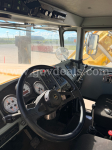 Cab interior of 2012 Oshkosh FWD truck showing steering wheel, gauges, and controls; view through windshield with exterior equipment visible.