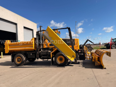 Oshkosh forward-control plow truck with yellow body and attachment, side view showing snowplow blade and hydraulic components.