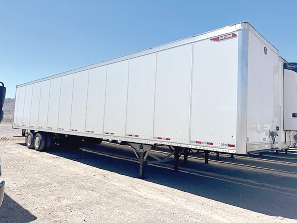 Trailer side view showing a long white dry van trailer with tandem axles and a raised landing gear.