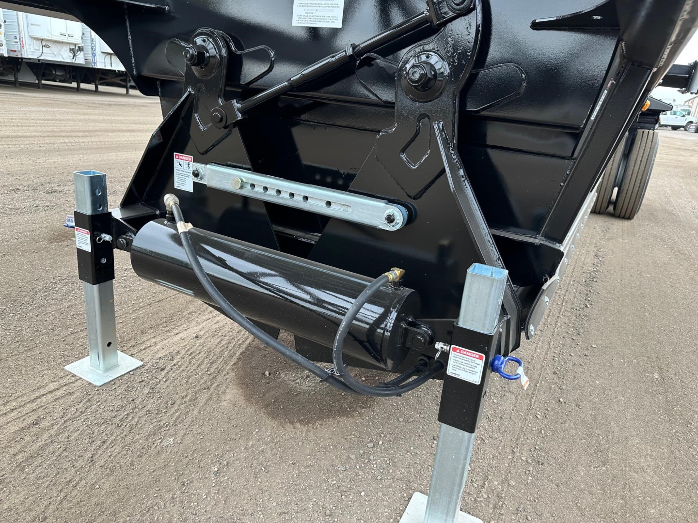 Bottom-dump trailer hitch area showing hydraulic cylinder and support legs with labels and wiring