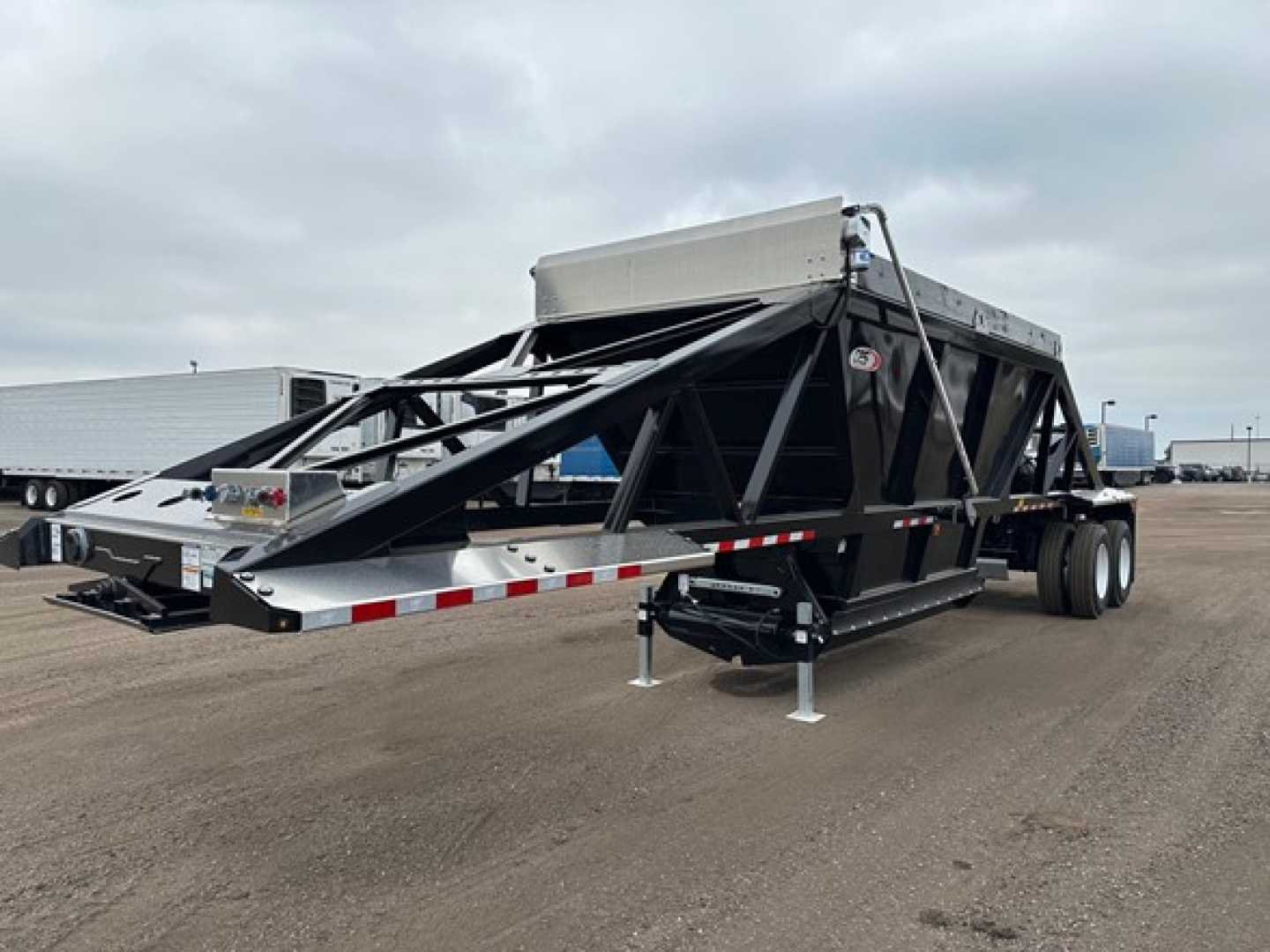Bottom dump trailer with lightweight, open-frame steel structure and hydraulic dump mechanism, dual axle, ramped tail section, and front storage box.