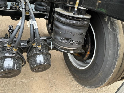 Bottom dump trailer undercarriage showing axles, air tanks, and wheel with tire. Visible are multiple cylindrical air reservoirs and a large round air tank mounted near the frame.