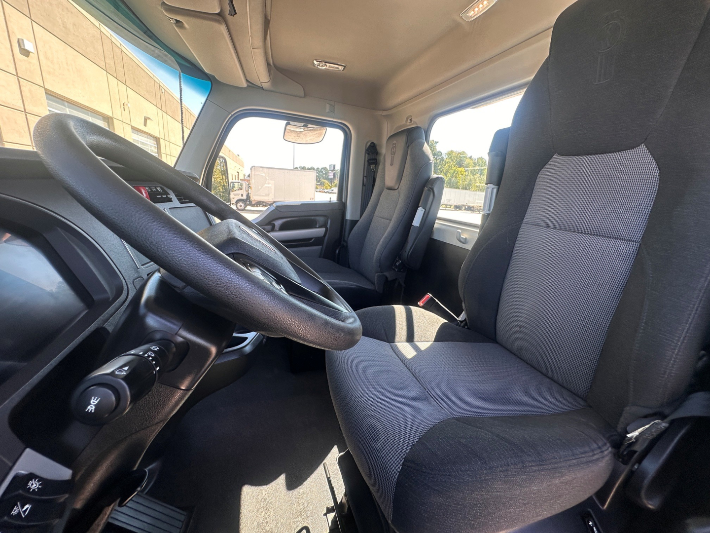 Kenworth T880 truck cabin interior with steering wheel and driver seat visible, gray fabric seats, dashboard, and front windshield.