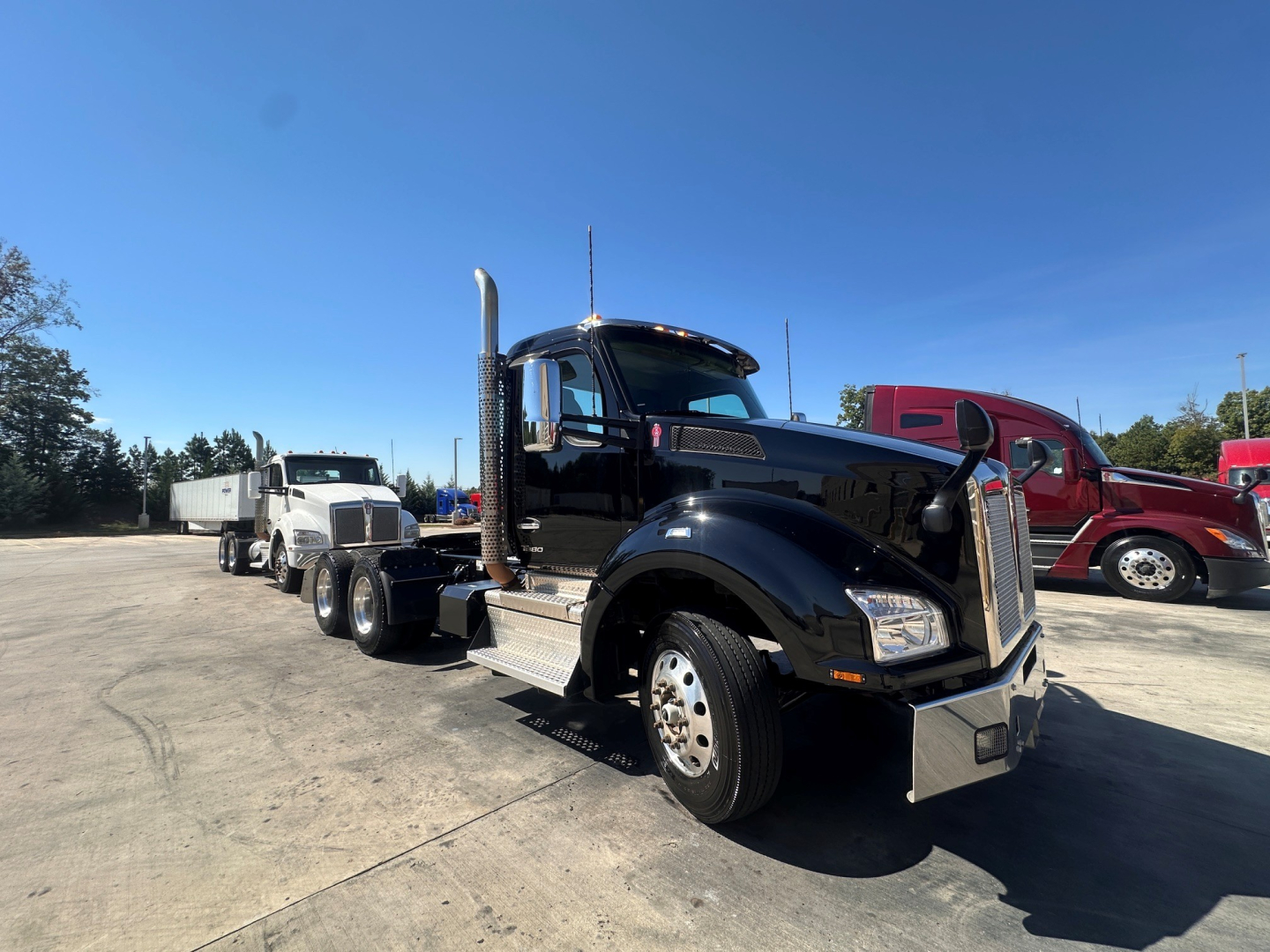 Kenworth T880 conventional daycab truck in a parking lot, black exterior, chrome exhaust stacks, front right angled view.