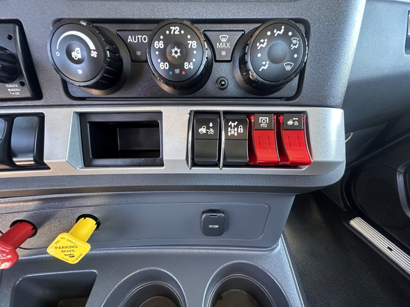 Kenworth T880 dashboard center console showing climate controls and row of red toggle switches, cup holders, and dashboard storage below.