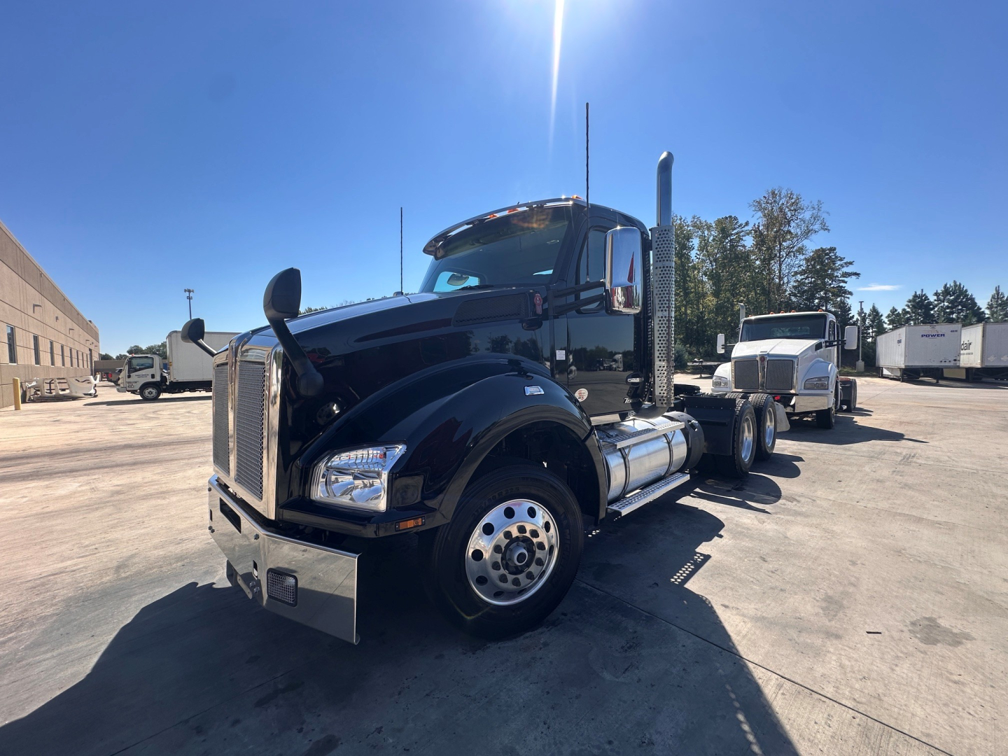 Kenworth T880 daycab tractor viewed from front-left in a truck yard showing chrome fuel tanks and tall exhaust stacks.