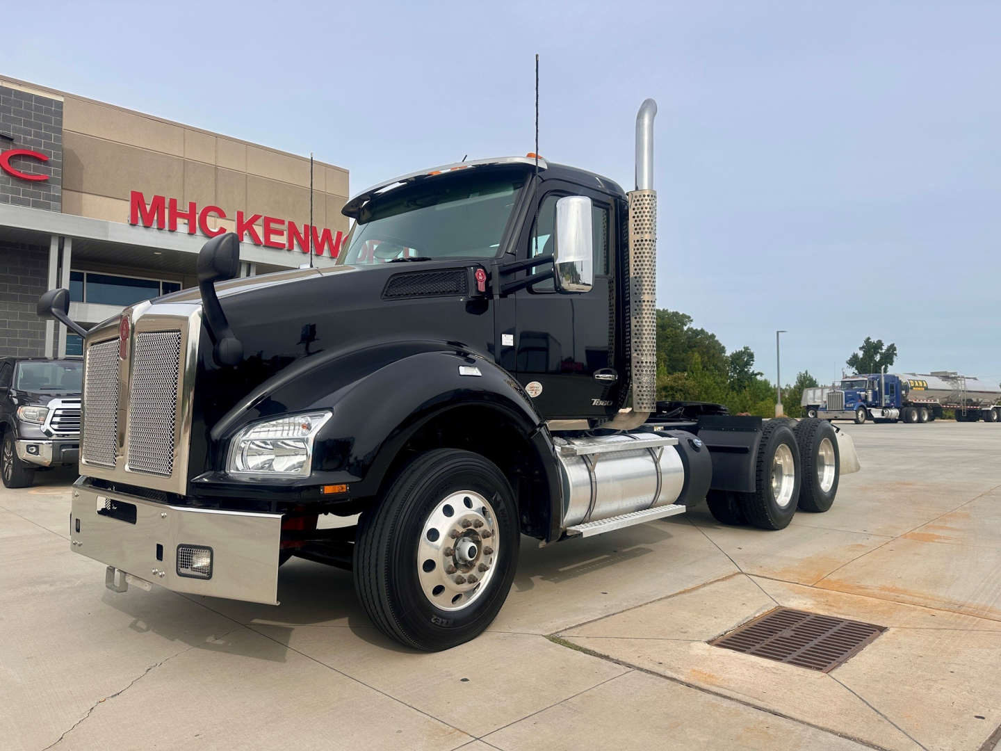 Kenworth T880 daycab tractor showing chrome exhaust stack and fuel tanks with front bumper, black cab, and dual rear axles.