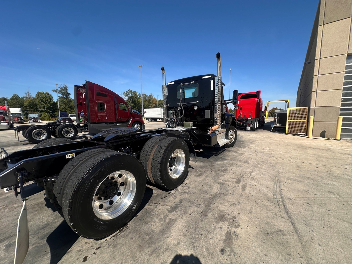 Kenworth T880 daycab tractor chassis with dual rear axles and cab in front of a service area; multiple trucks in background.