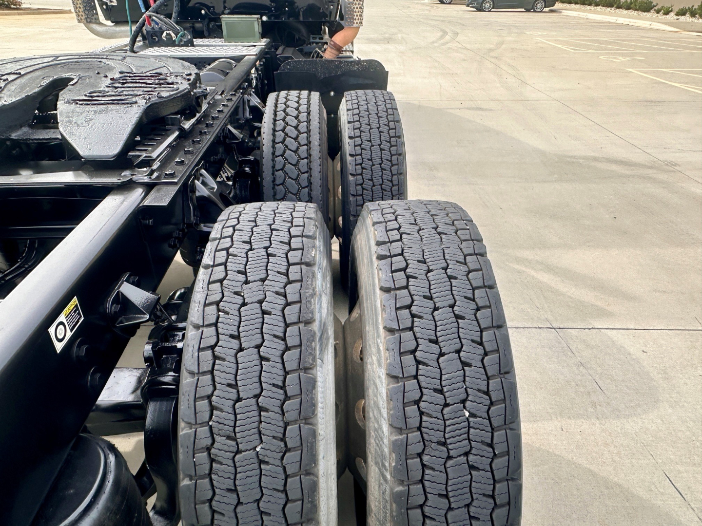 Kenworth T880 chassis showing dual rear axles and tire tread pattern; view focuses on the wheel pair area near the cab with nearby frame and suspension components visible.
