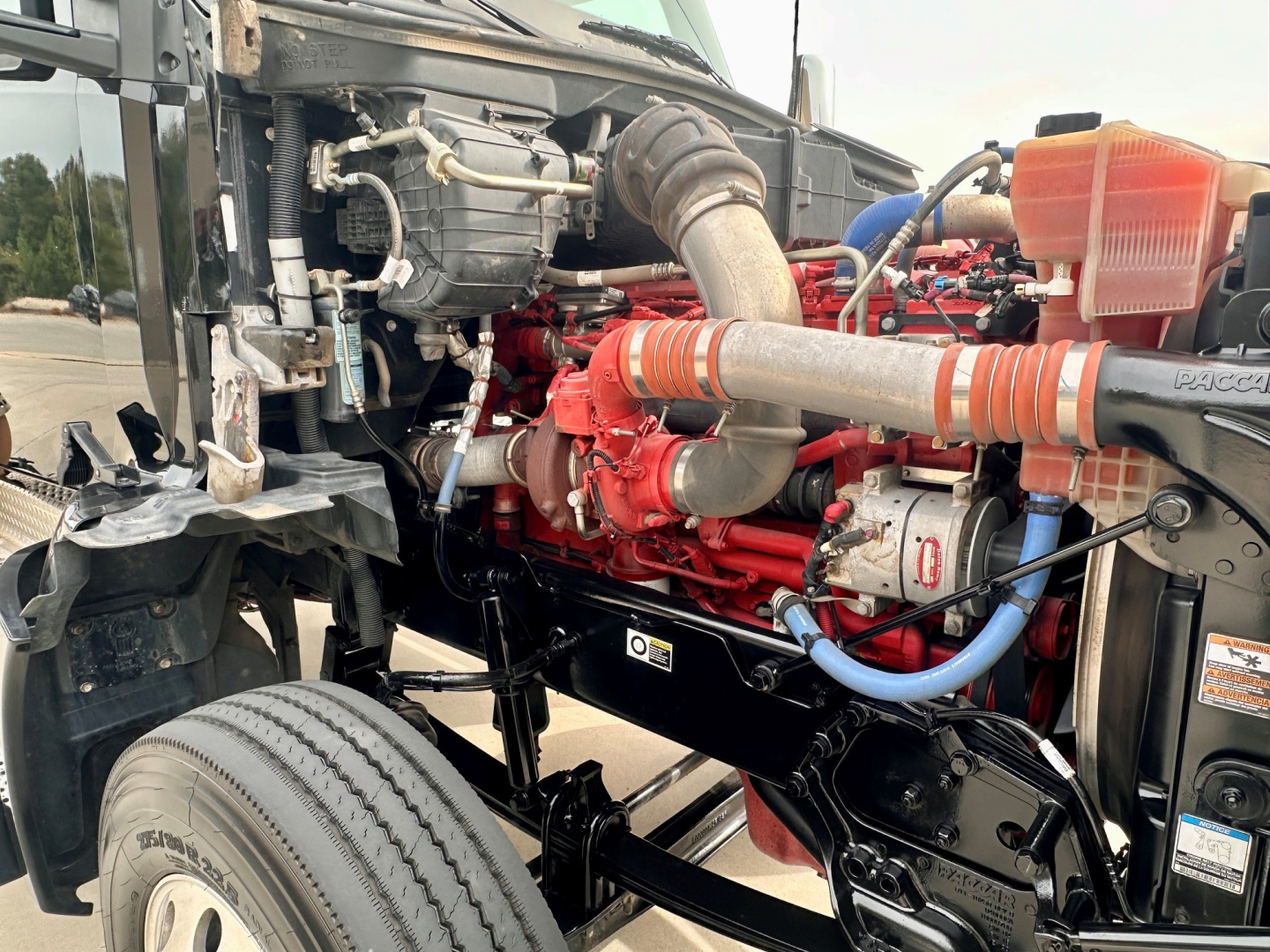 Kenworth T880 engine bay showing red engine and intake piping with hoses, coolant reservoir, and front chassis.