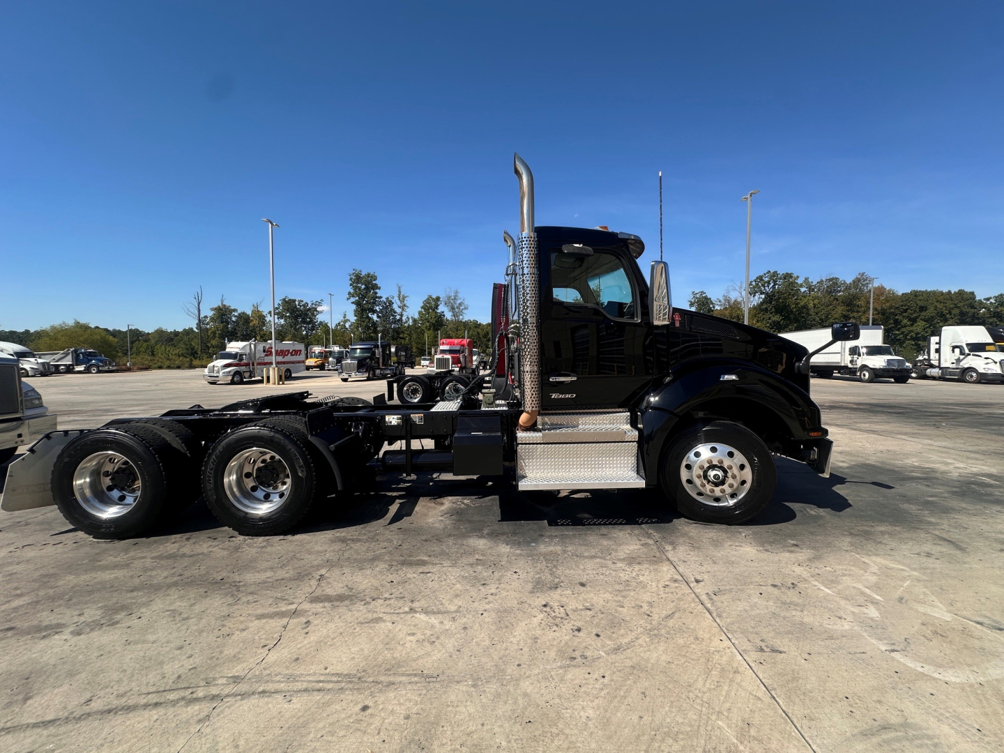 Kenworth T880 daycab truck side view showing black cab, chrome exhaust stack, aluminum steps, dual rear axles, and fifth wheel undercarriage.
