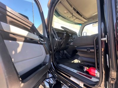 Kenworth T880 truck cab interior with open driver door showing seats and dashboard; floor entry with ladder steps and a small red fire extinguisher near the seat.