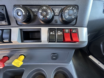 Kenworth T880 dashboard center console showing climate controls and row of red toggle switches, cup holders, and dashboard storage below.