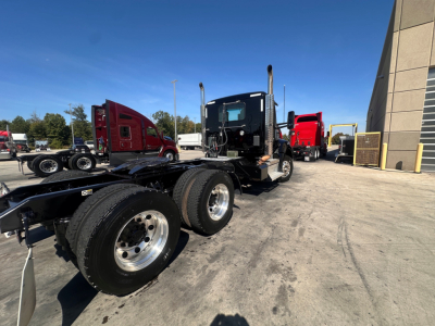 Kenworth T880 daycab tractor chassis with dual rear axles and cab in front of a service area; multiple trucks in background.