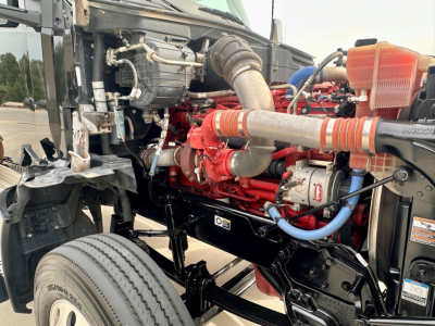 Kenworth T880 engine bay showing red engine and intake piping with hoses, coolant reservoir, and front chassis.