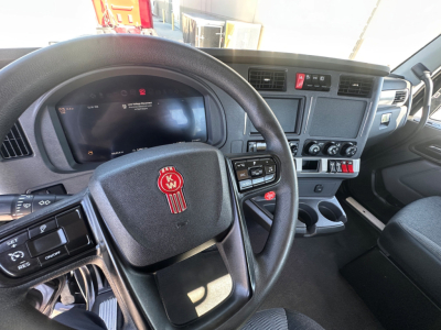 Kenworth T880 cab interior showing steering wheel with Kenworth logo and instrument cluster, center console with controls and cup holders.