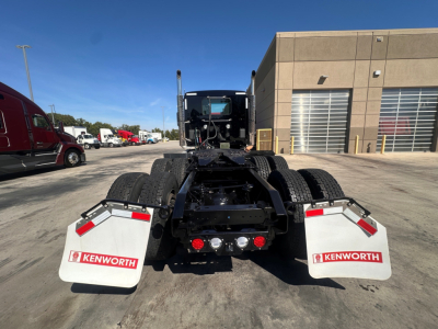 Kenworth T880 chassis and rear view showing mud flaps with Kenworth logos, fifth wheel mounting, and dual rear axles in a truck yard.
