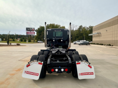 Kenworth T880 rear view showing dual rear axles, mud flaps with Kenworth logos, and fifth wheel mount in a parking lot.