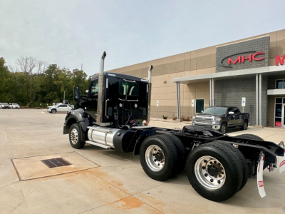 Kenworth T880 tractor cab chassis showing side view, dual rear axles, fuel tanks, and exhaust stacks in a dealership lot.