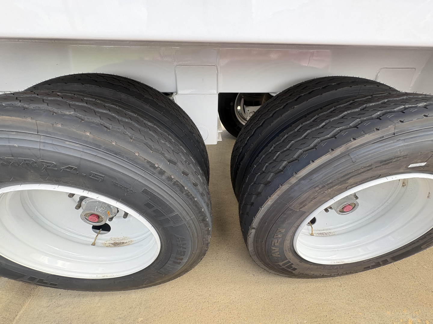 Two rear dual tires of a trailer showing white wheels and black tires with rims.