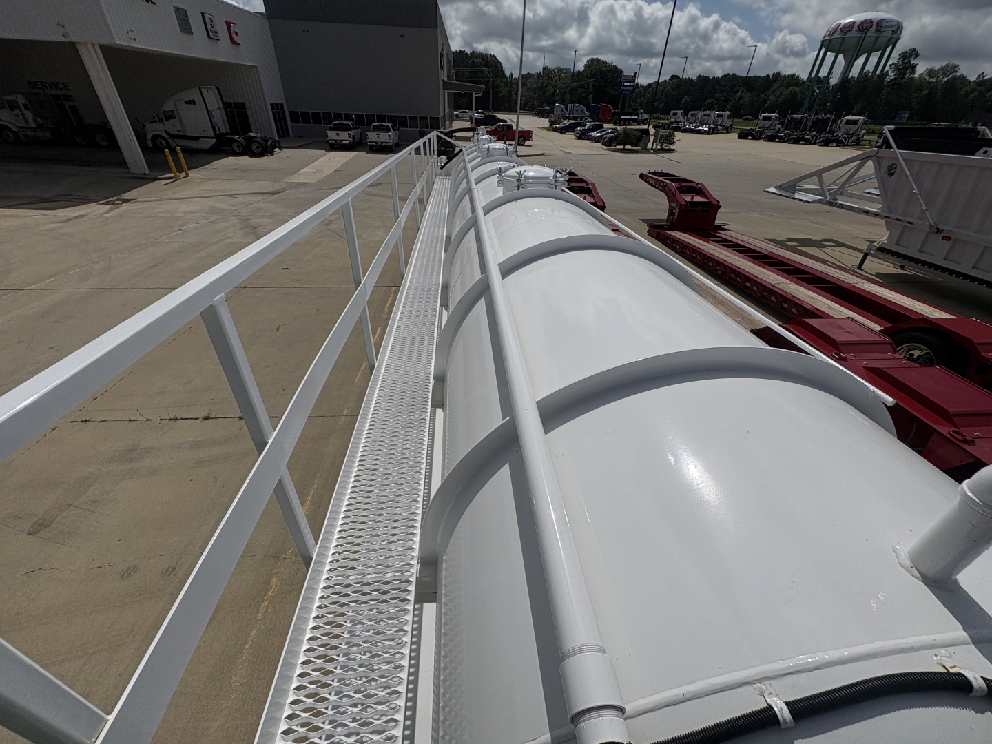 Vacuum trailer top rail with rounded white tank sections and safety railing; long perspective shot at a dealership lot.