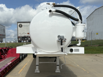 Tank trailer back view showing large white cylindrical tank with black hoses, control panel, and mounted auxiliary unit on a white trailer chassis.