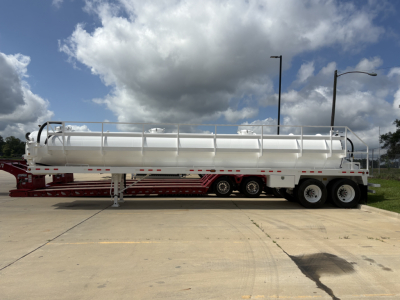 Tank trailer in-service side view showing cylindrical stainless steel tank with railing, mounted on tandem axle trailer with support legs.
