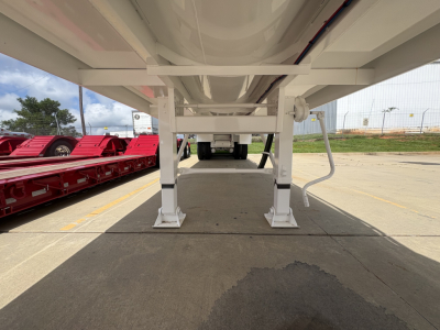 Trailer underside view showing support legs and frame with white-painted steel, undercarriage of a Troxell 130BBL trailer, outboard red trailers in background.