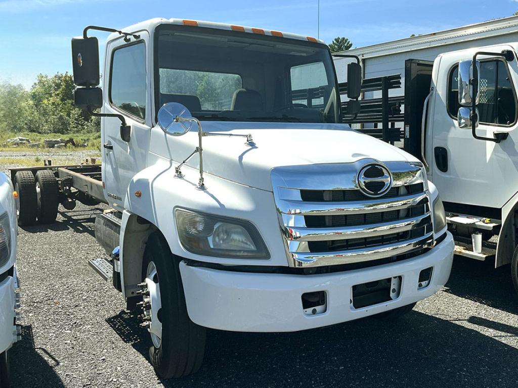 Hino 338 cab and chassis truck front view showing white cab, chrome grille, rectangular headlights, side mirrors, and windshield.