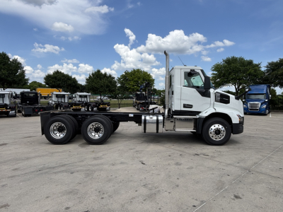 Truck chassis and cab of a 2027 Mack AN64 dump truck, side view with white cab and dual rear axles on a dealership lot.