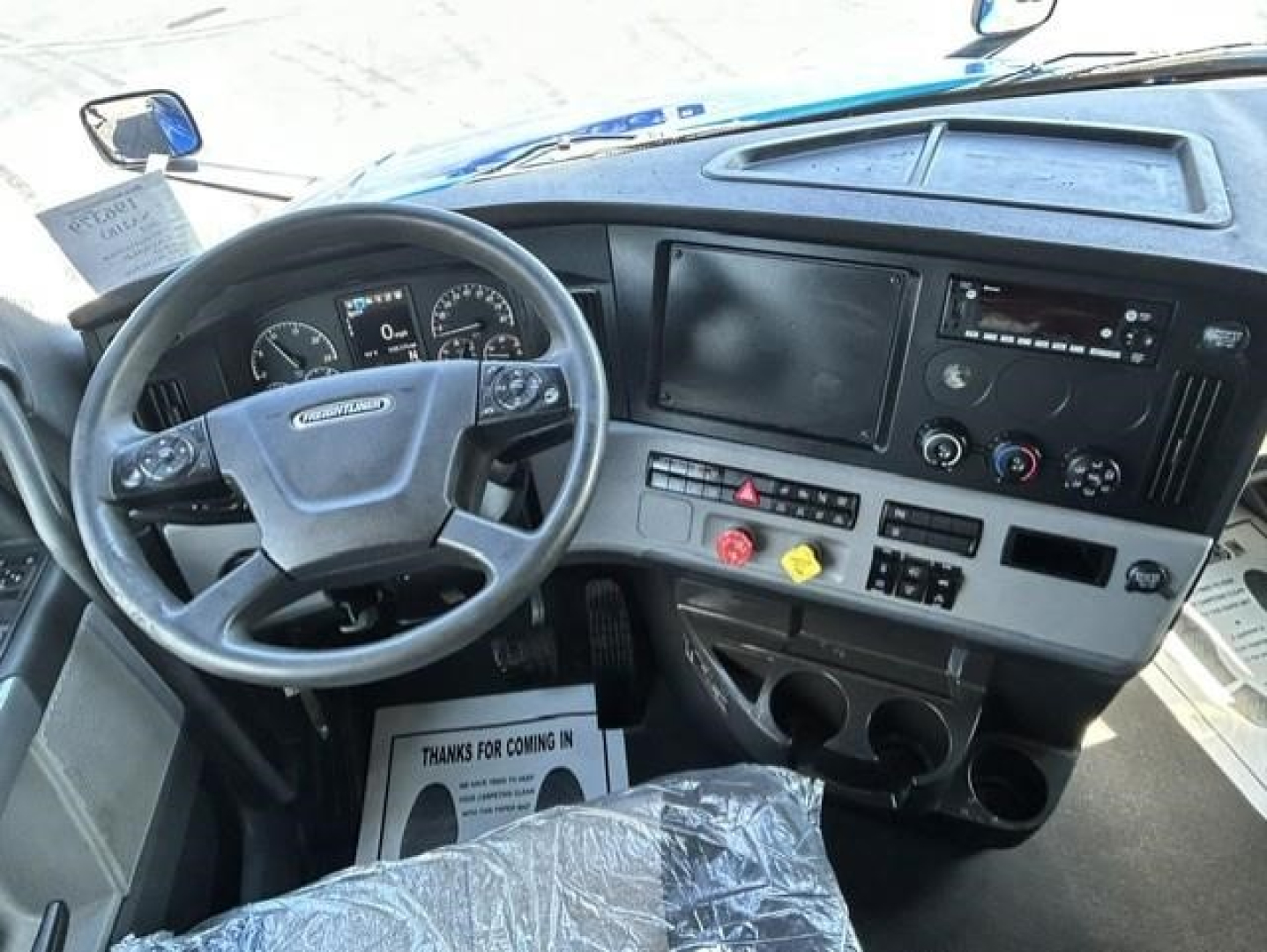 Truck cab interior showing steering wheel, dashboard with digital display screens, control panel, and cup holders.