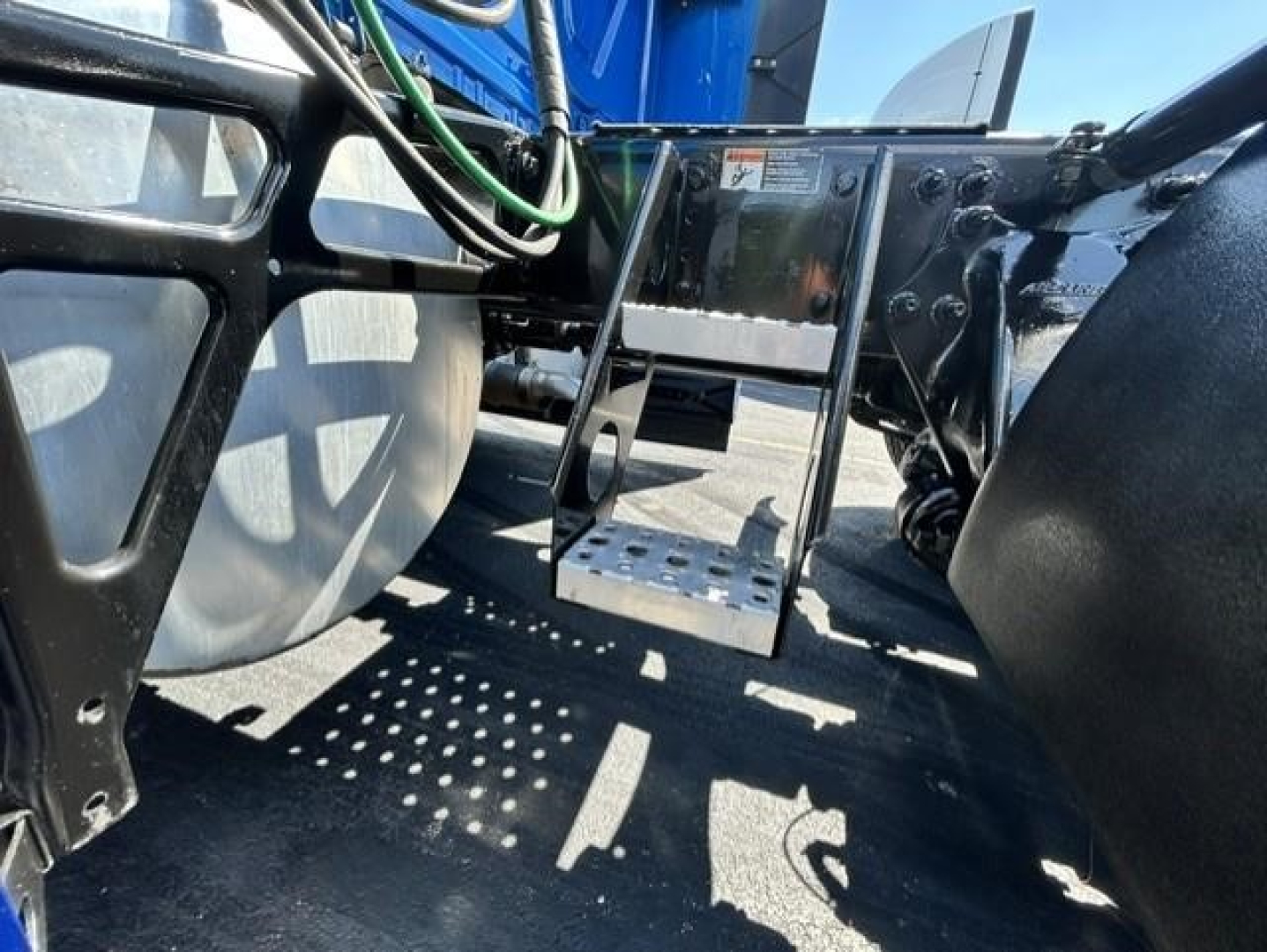 Freightliner Cascadia 126 chassis area showing access steps and undercarriage components. Visible are metal step platform, frame rails, hoses, and part of wheel and air lines.