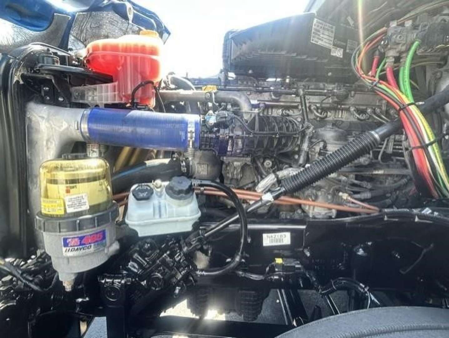 Freightliner Cascadia engine bay showing coolant reservoir, oil filter, and various hoses and wiring in the engine compartment.