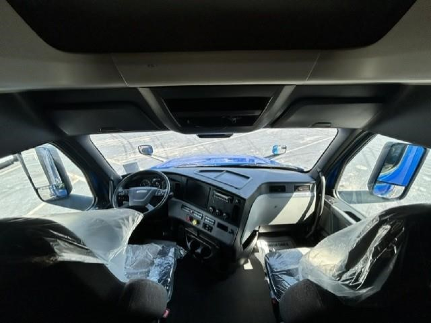 Cab interior of a Freightliner Cascadia 126 truck showing steering wheel, dashboard, and front seats wrapped in plastic.
