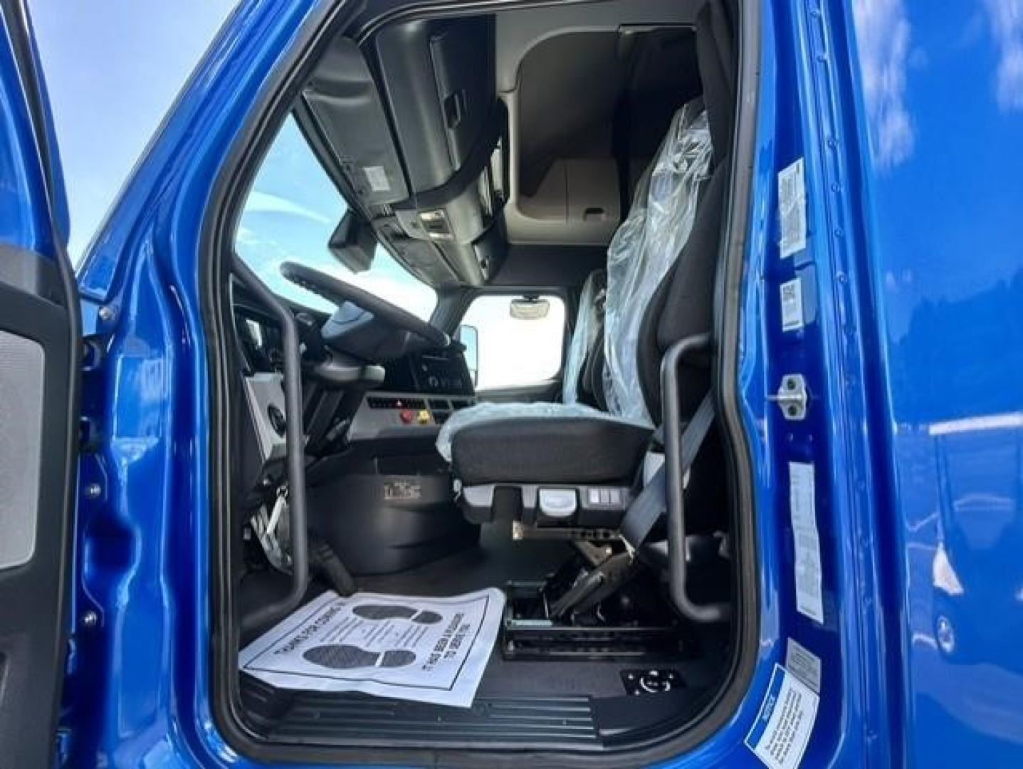 Freightliner Cascadia 126 cab interior with steering wheel and driver seat visible through open door.