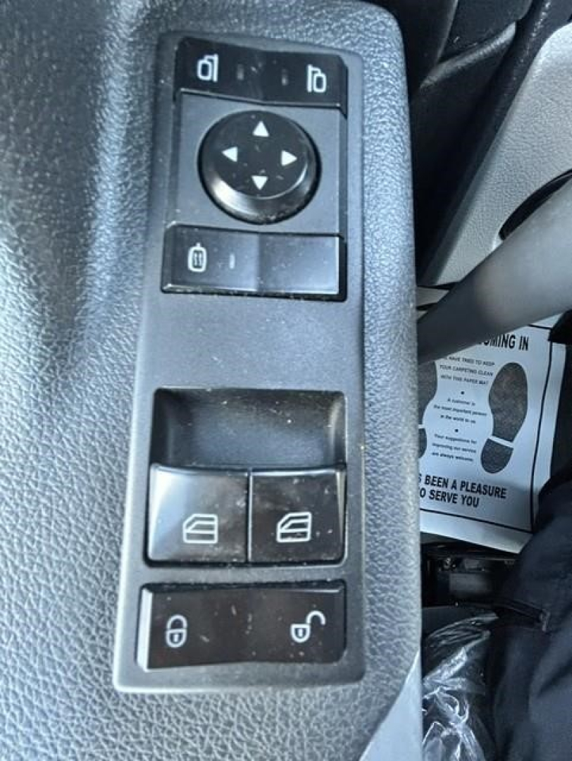 Control panel with window/mirror adjustment pad and lock/unlock switches inside a Freightliner Cascadia cab. Visible buttons include a circular directional pad with four arrows, two small rectangular buttons above, two window control switch