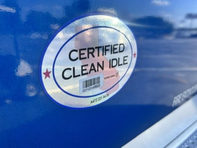 Sticker reads CERTIFIED CLEAN IDLE on blue Freightliner Cascadia door panel with barcode tag.