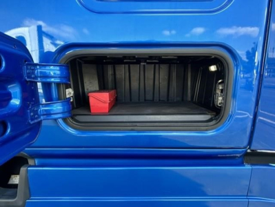 Freightliner Cascadia 126 cab storage compartment open showing empty cargo bay with a small red toolbox.