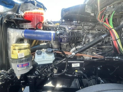 Freightliner Cascadia engine bay showing coolant reservoir, oil filter, and various hoses and wiring in the engine compartment.