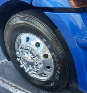 Truck front wheel well showing a polished chrome wheel with multiple lug nuts on a blue Freightliner Cascadia 126; tire sidewall shows tire model and branding.