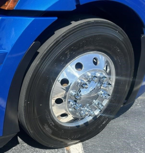 Freightliner Cascadia front wheel and tire close-up showing polished steel hub and Rim. Visible tire sidewall with manufacturer markings.