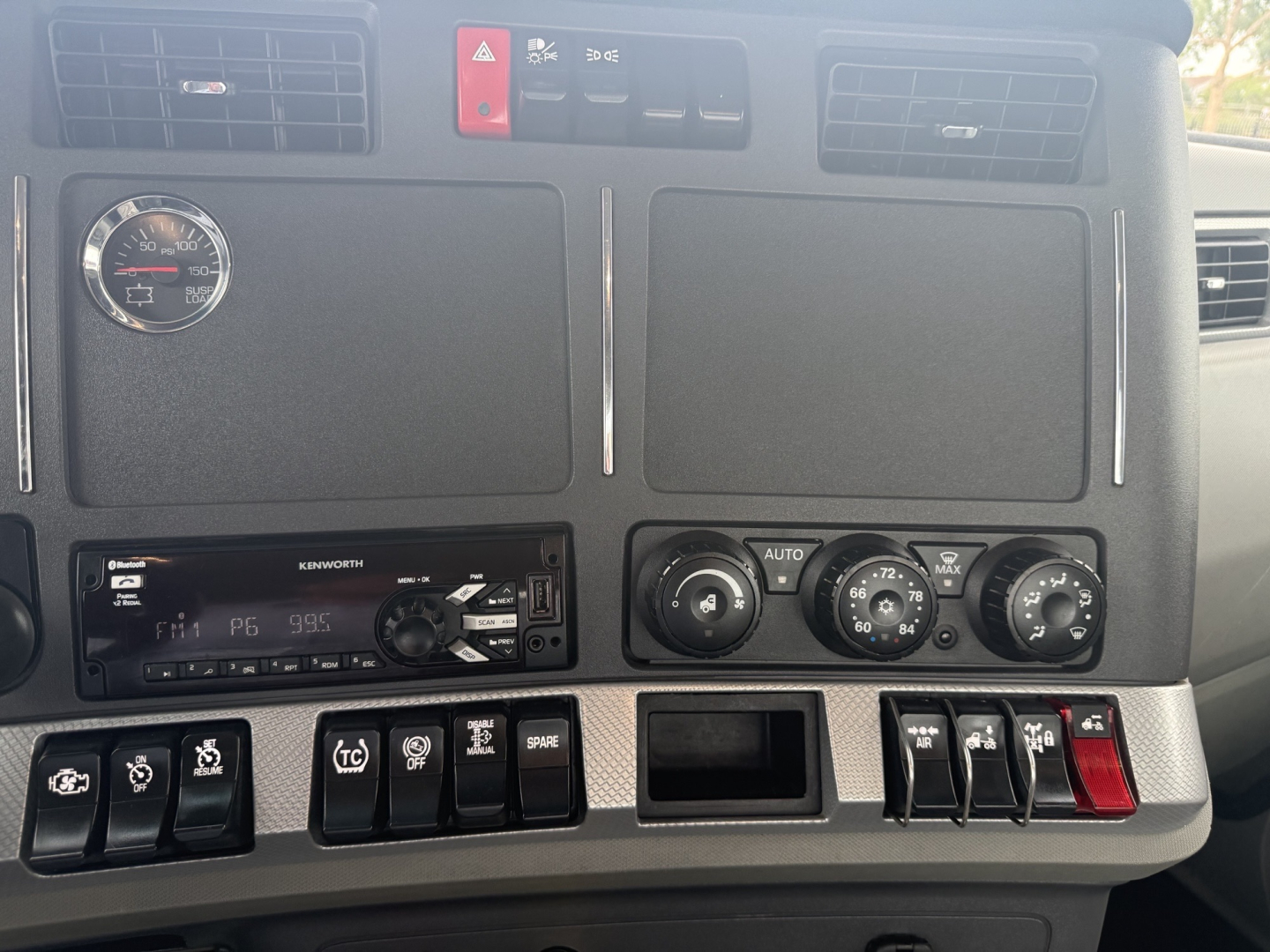 Dashboard of a Kenworth T680 showing a round gauge, two large vent panels, controls, and a Kenworth radio/display; multiple switches and climate controls visible.