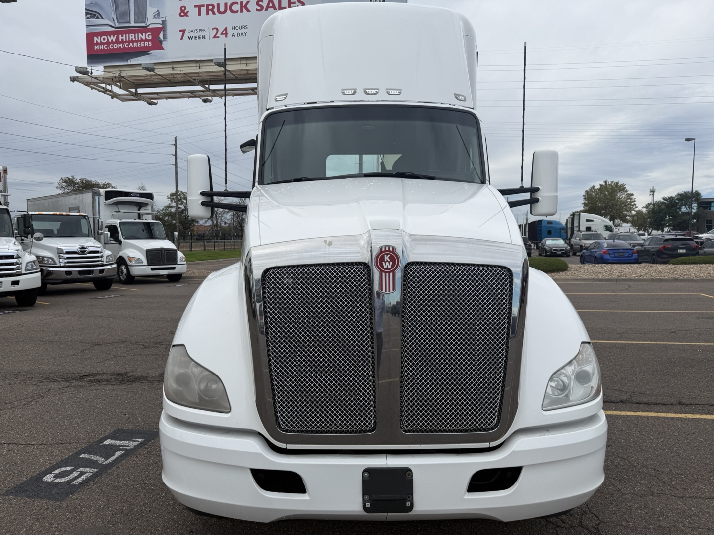 Kenworth T680 front view showing large grille, white cab, side mirrors, and bumper. VIN and stock number visible in listing; equipment appears in a dealership lot.