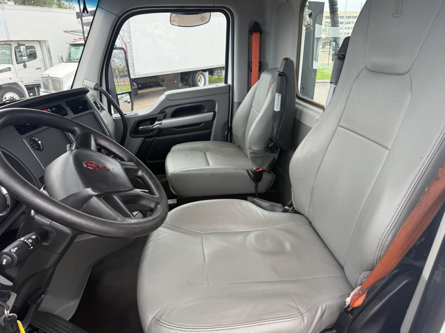Kenworth T680 cab interior showing grey cloth seats and steering wheel with dashboard.