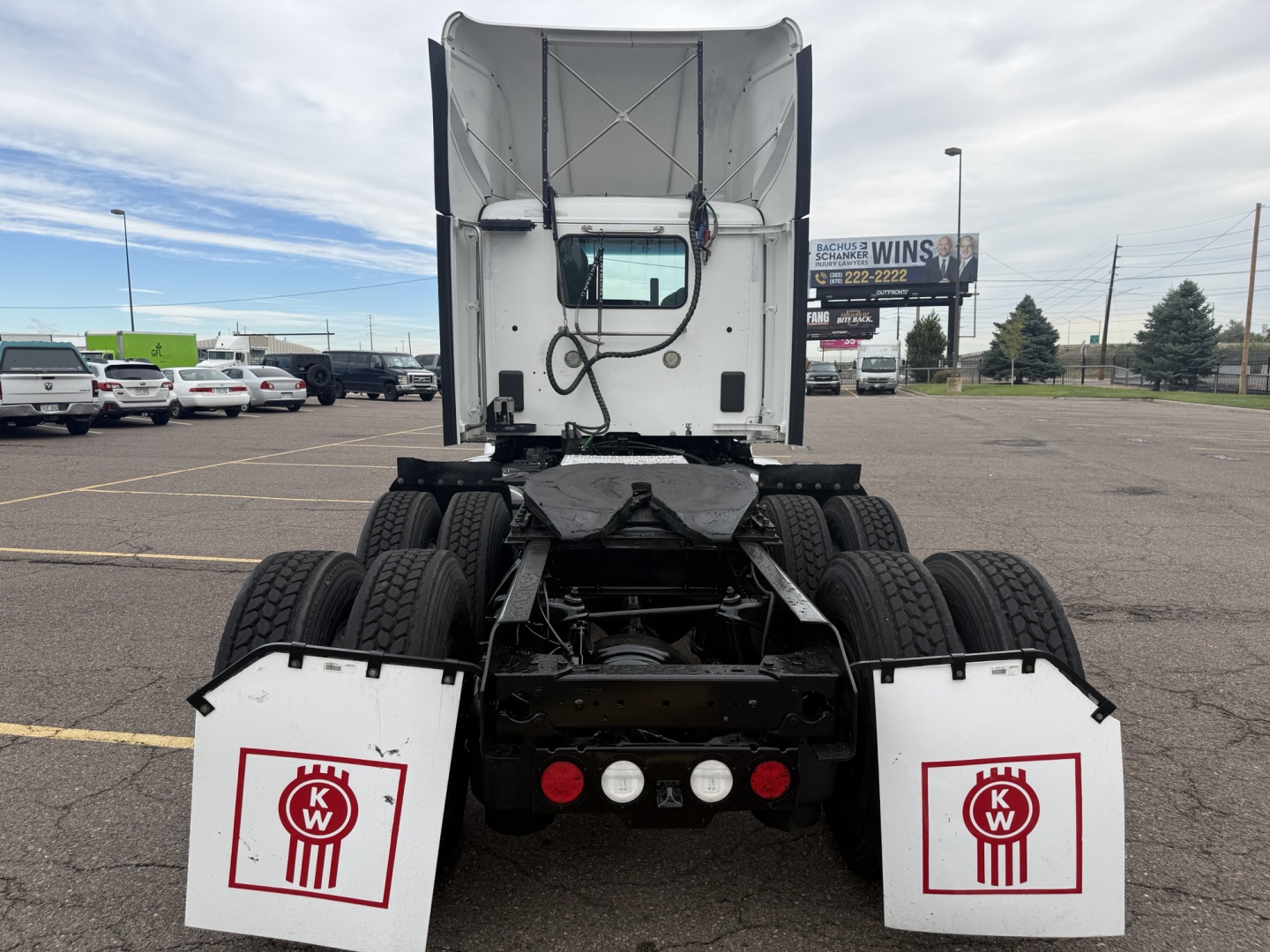 Kenworth T680 rear view showing fifth wheel, dual rear axles, white KW mudflaps with red KW logo, and truck cab in background.