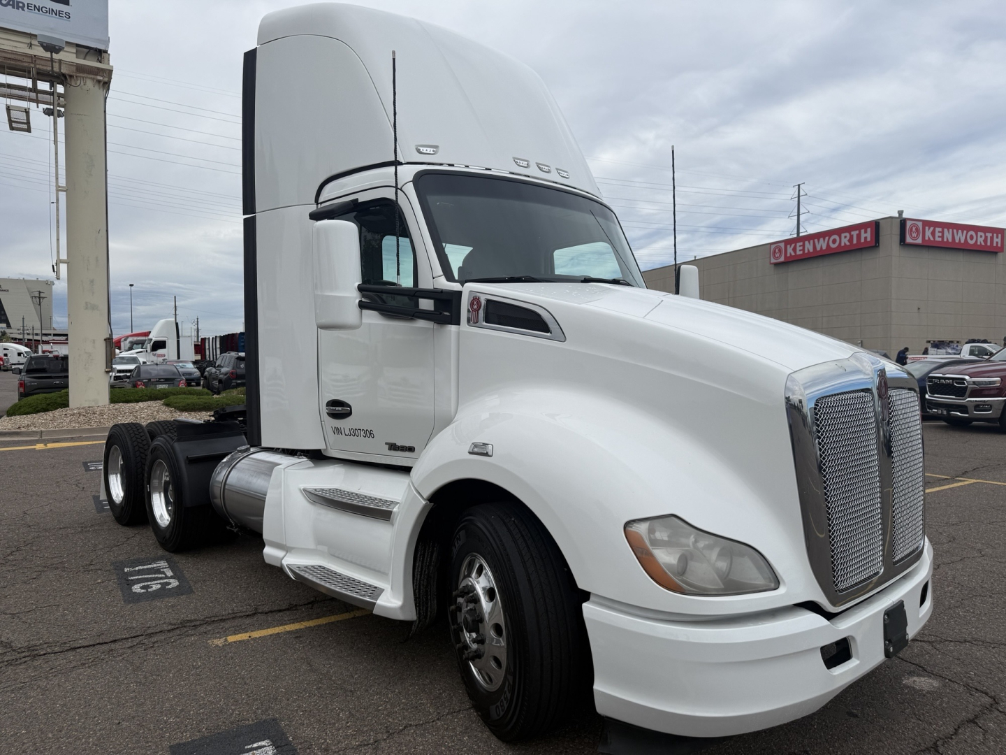 Kenworth T680 truck tractor in a parking lot, white cab, sleeper, dual rear axles, chrome grille, front fender markers, factory badging visible.