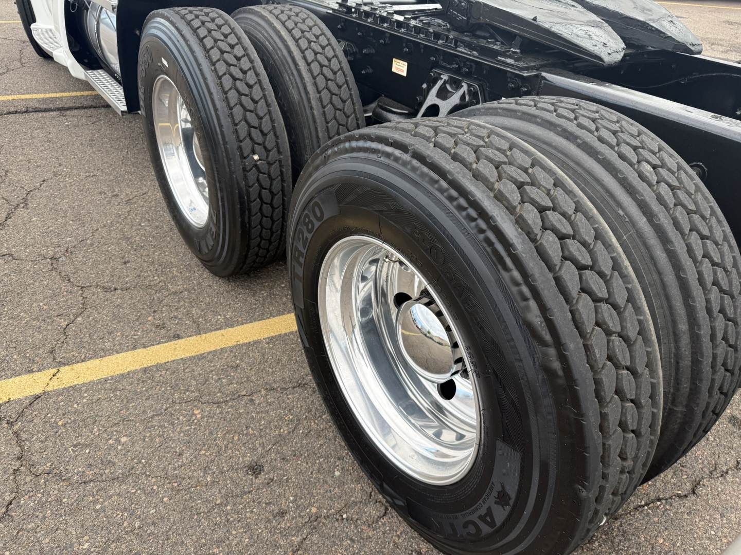 Kenworth T680 wheel area showing dual rear axles with large Michelin or similar tires, chrome rims, truck chassis and frame visible.