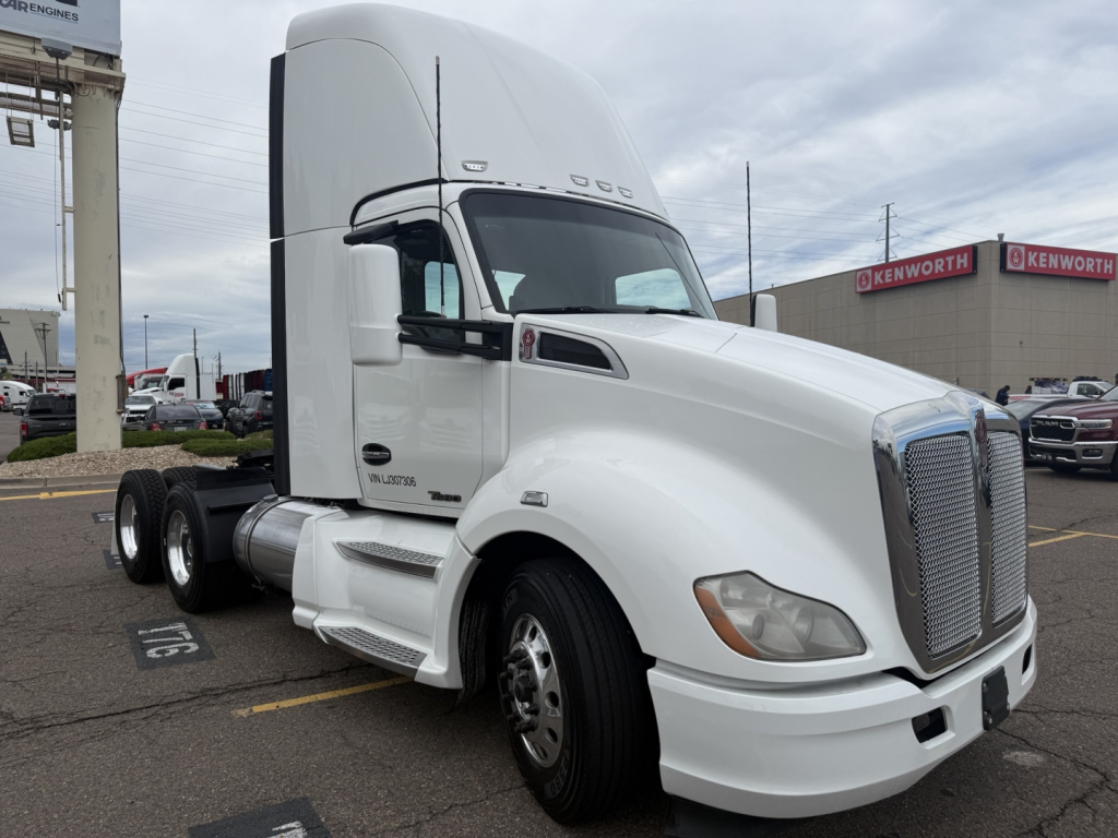 Kenworth T680 truck tractor in a parking lot, white cab, sleeper, dual rear axles, chrome grille, front fender markers, factory badging visible.
