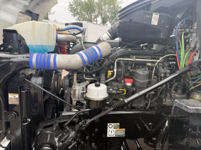 Kenworth T680 engine bay showing coolant reservoir, air intake, hoses, and various wiring harnesses.