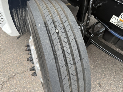 Kenworth T680 front wheel and tire close-up showing dual rear? axles and wheel hub, with tread pattern on highway tire.